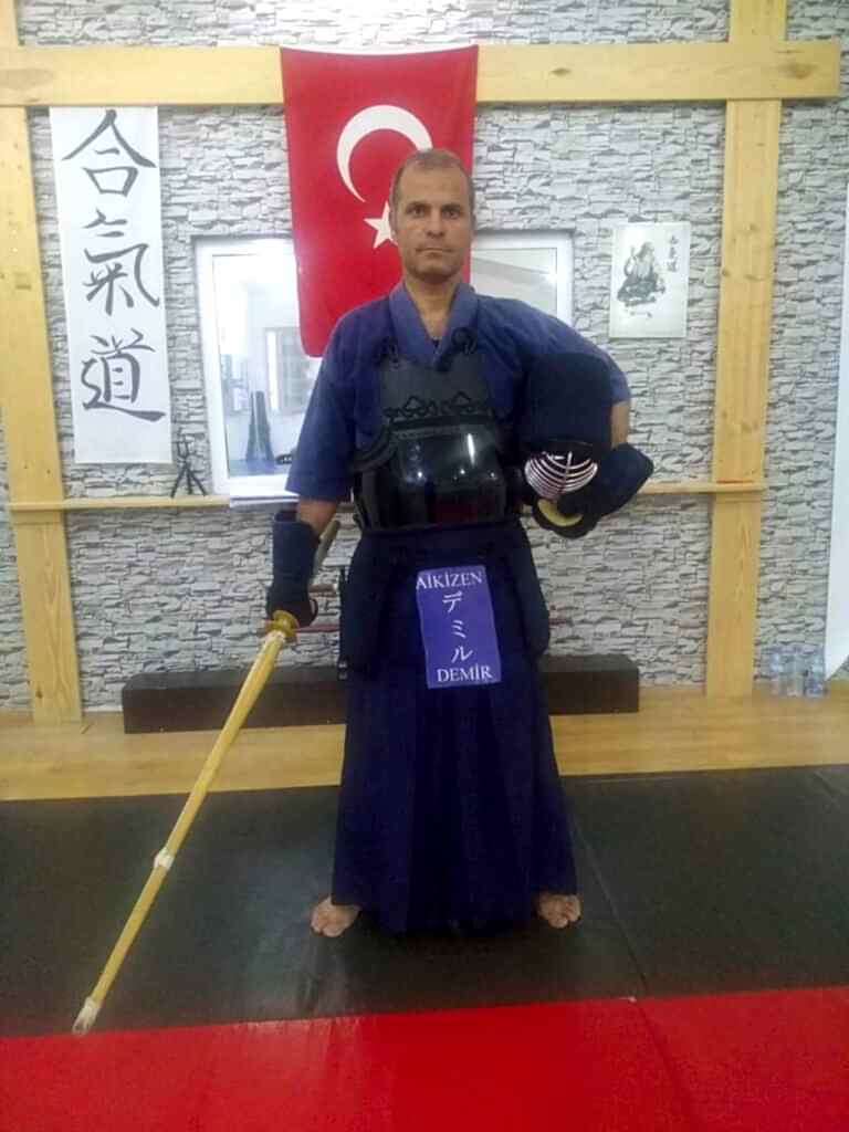 Kürşat Demir, geleneksel Kendo giysisi (keikogi ve hakama) ve zırhı (bogu) ile bir shinai tutarken bir dojo'da poz veriyor.